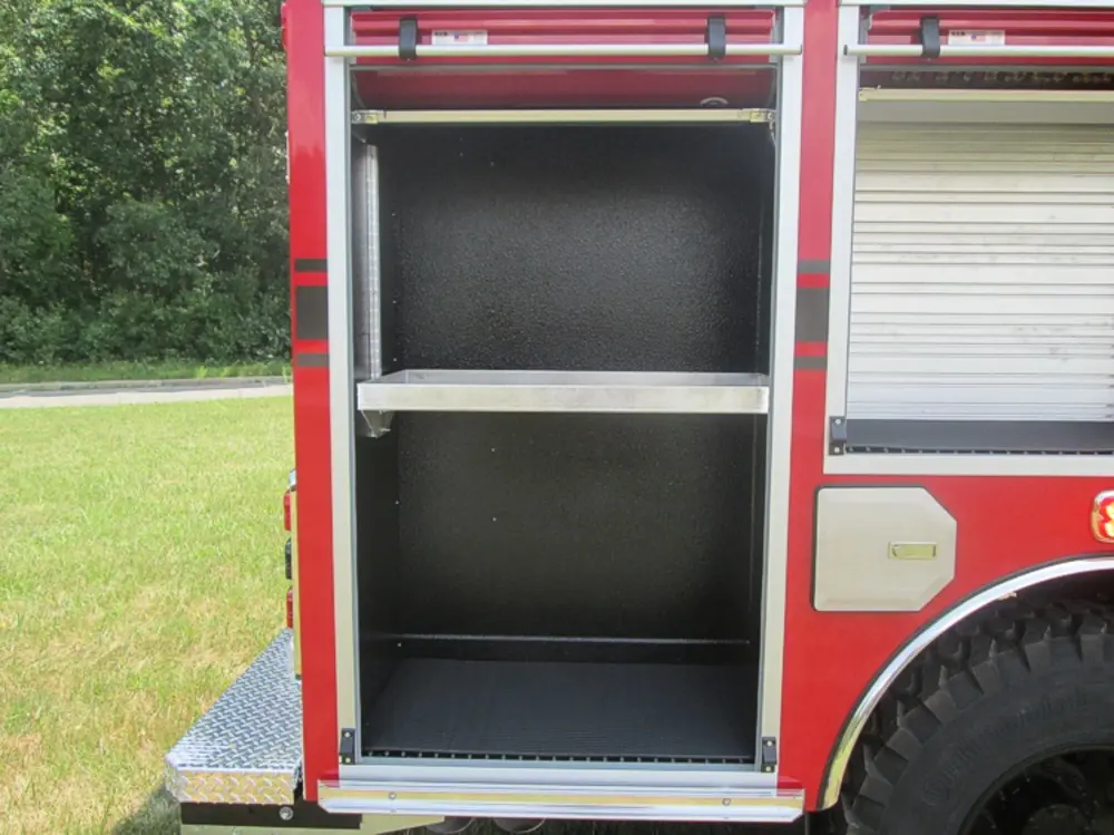 Exterior view of small fire truck showing cab, body compartments, and wheel/tire area.