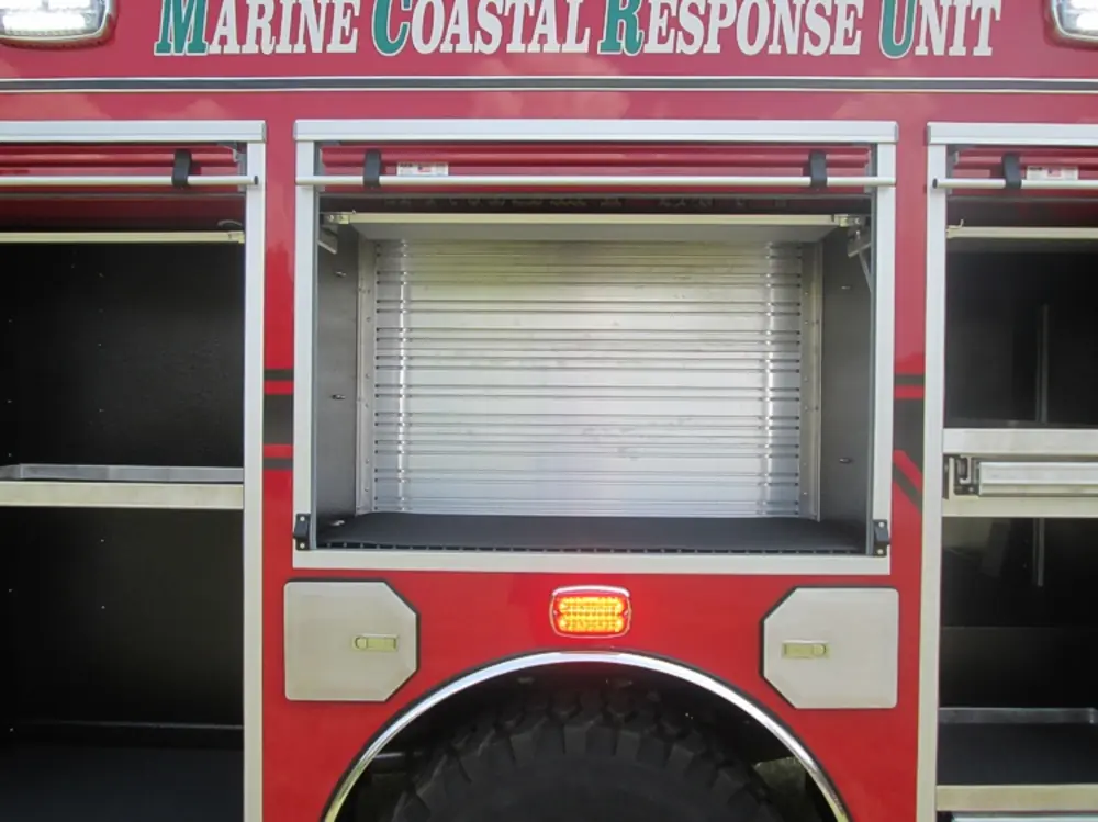 Exterior view of small fire truck showing cab, body compartments, and wheel/tire area.