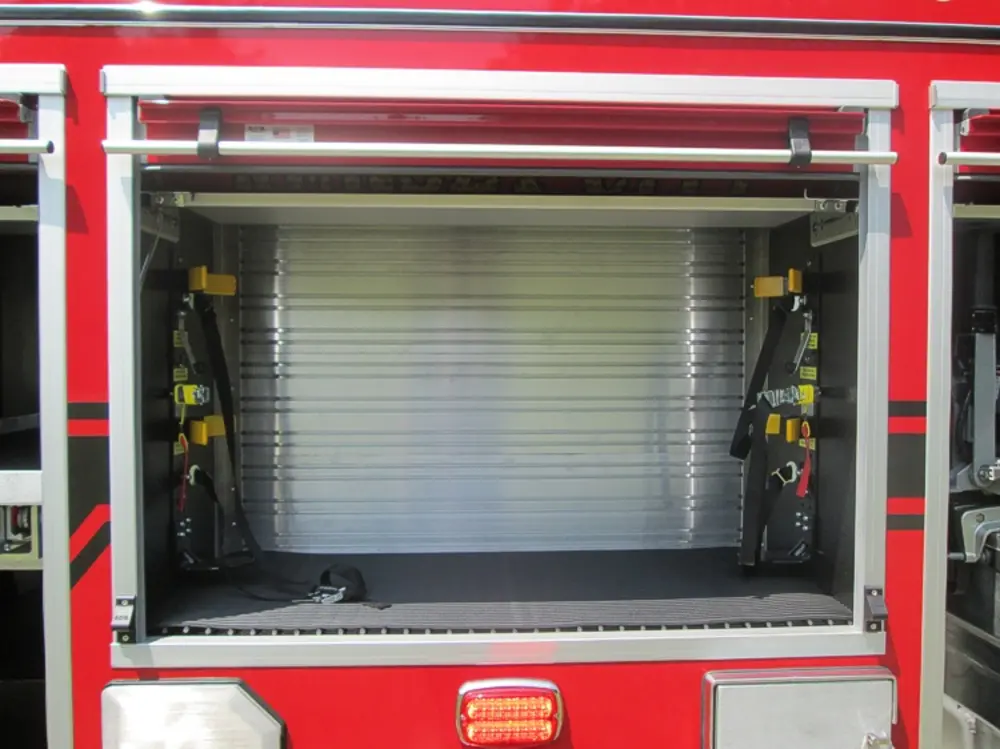 Exterior view of small fire truck showing cab, body compartments, and wheel/tire area.