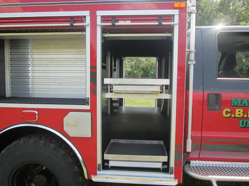 Exterior view of small fire truck showing cab, body compartments, and wheel/tire area.