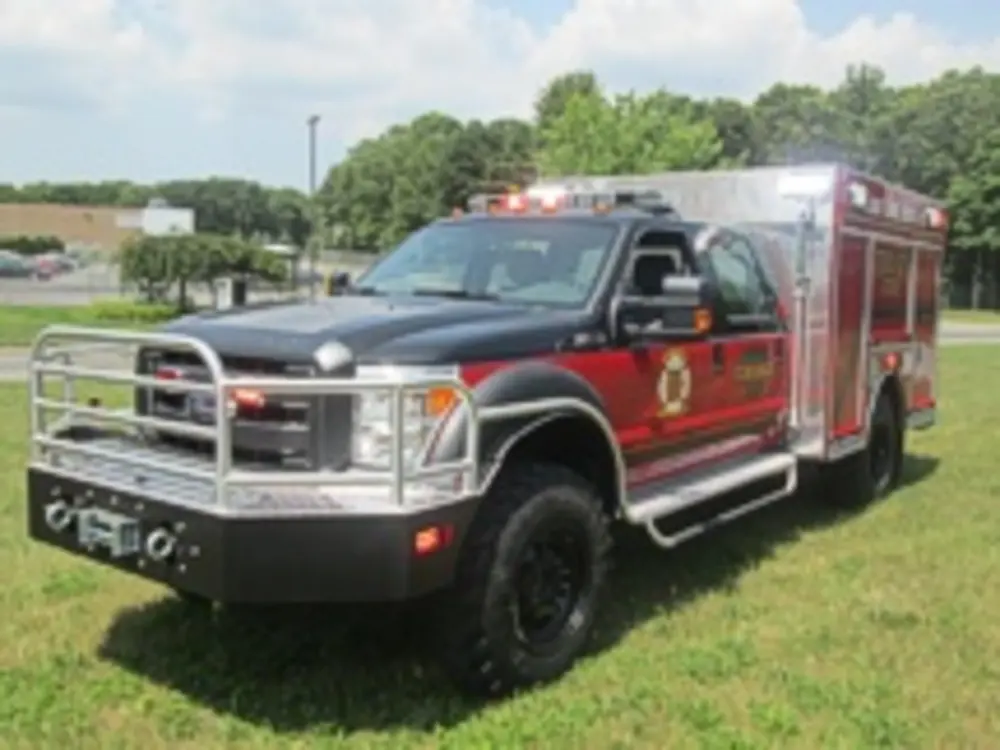 Exterior view of small fire truck showing cab, body compartments, and wheel/tire area.