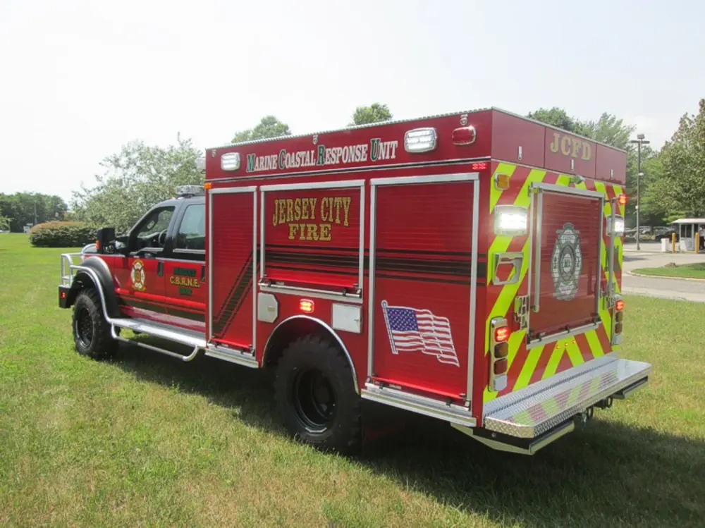 Exterior view of small fire truck showing cab, body compartments, and wheel/tire area.