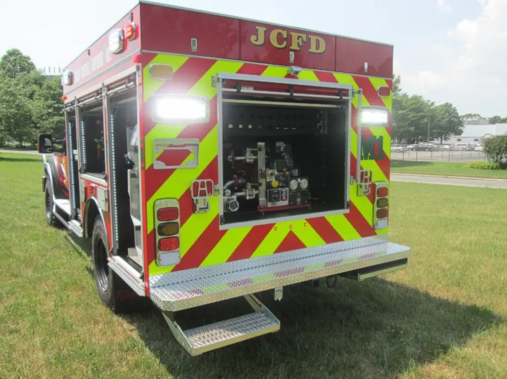 Exterior view of small fire truck showing cab, body compartments, and wheel/tire area.