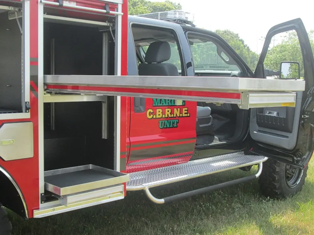 Exterior view of small fire truck showing cab, body compartments, and wheel/tire area.