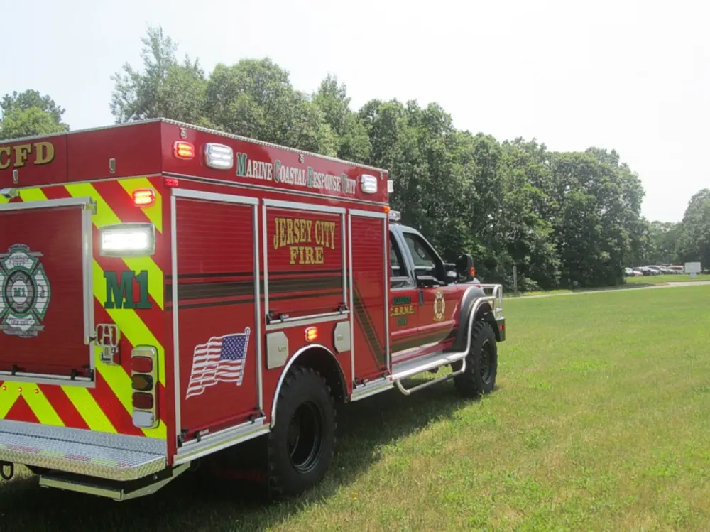 Exterior view of small fire truck showing cab, body compartments, and wheel/tire area.