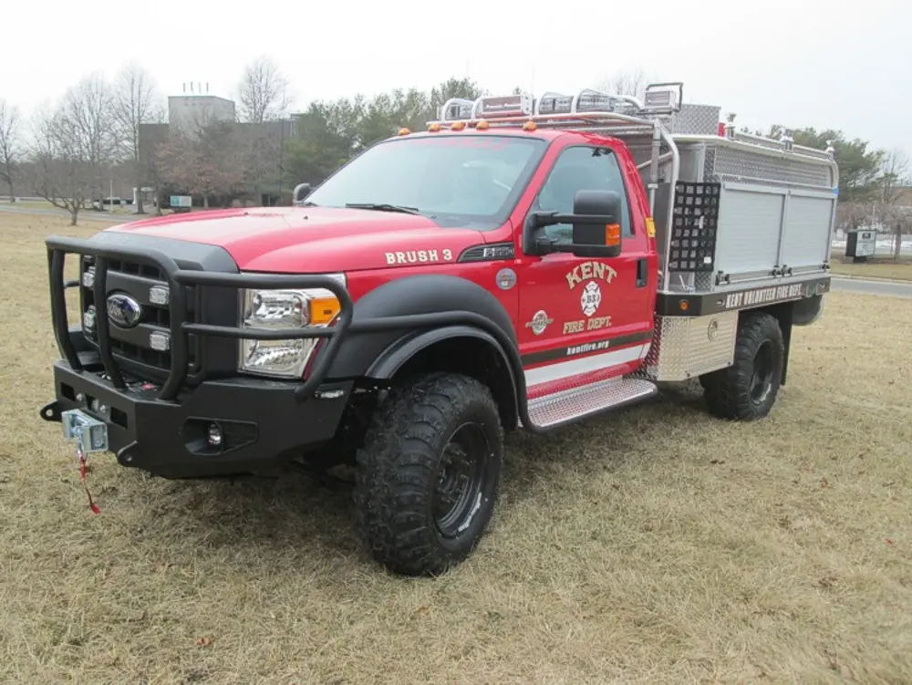 Exterior view of small fire truck showing cab, body compartments, and wheel/tire area.