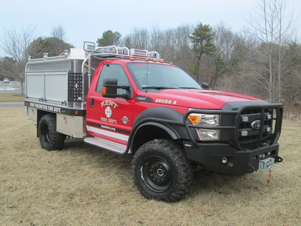 Exterior view of small fire truck showing cab, body compartments, and wheel/tire area.