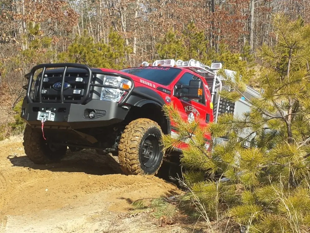 Exterior view of small fire truck showing cab, body compartments, and wheel/tire area.