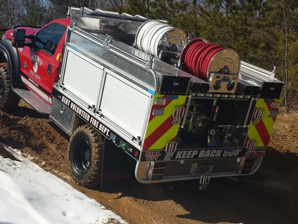 Exterior view of small fire truck showing cab, body compartments, and wheel/tire area.