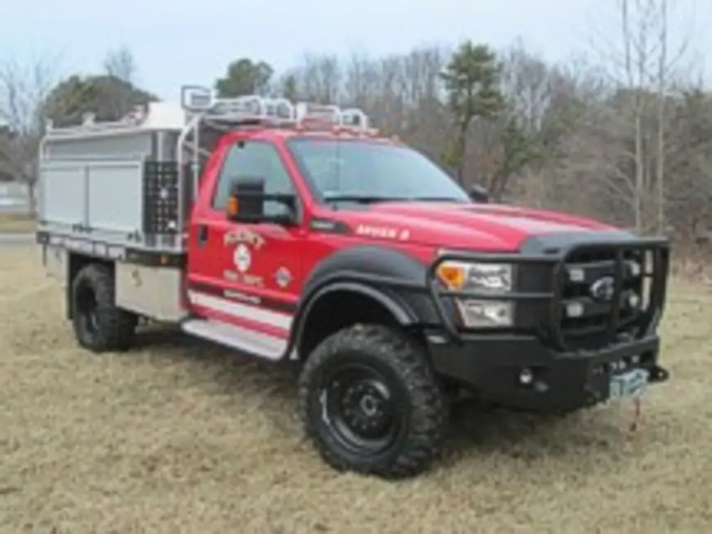 Exterior view of small fire truck showing cab, body compartments, and wheel/tire area.