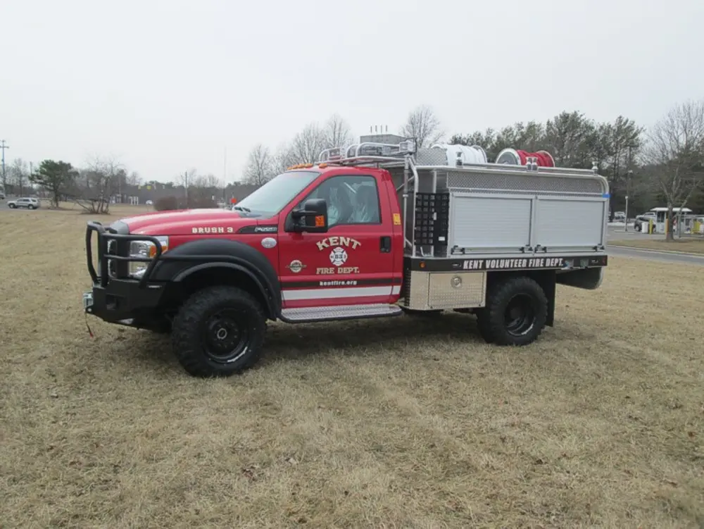 Exterior view of small fire truck showing cab, body compartments, and wheel/tire area.