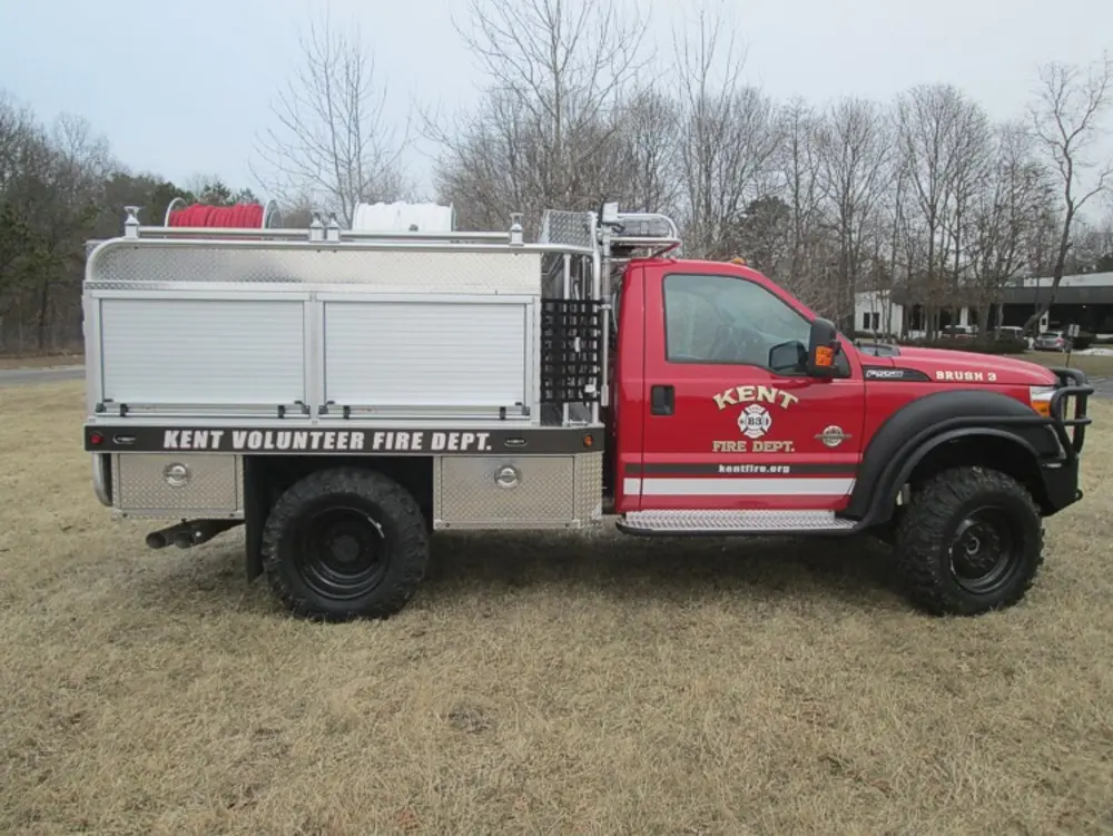 Exterior view of small fire truck showing cab, body compartments, and wheel/tire area.