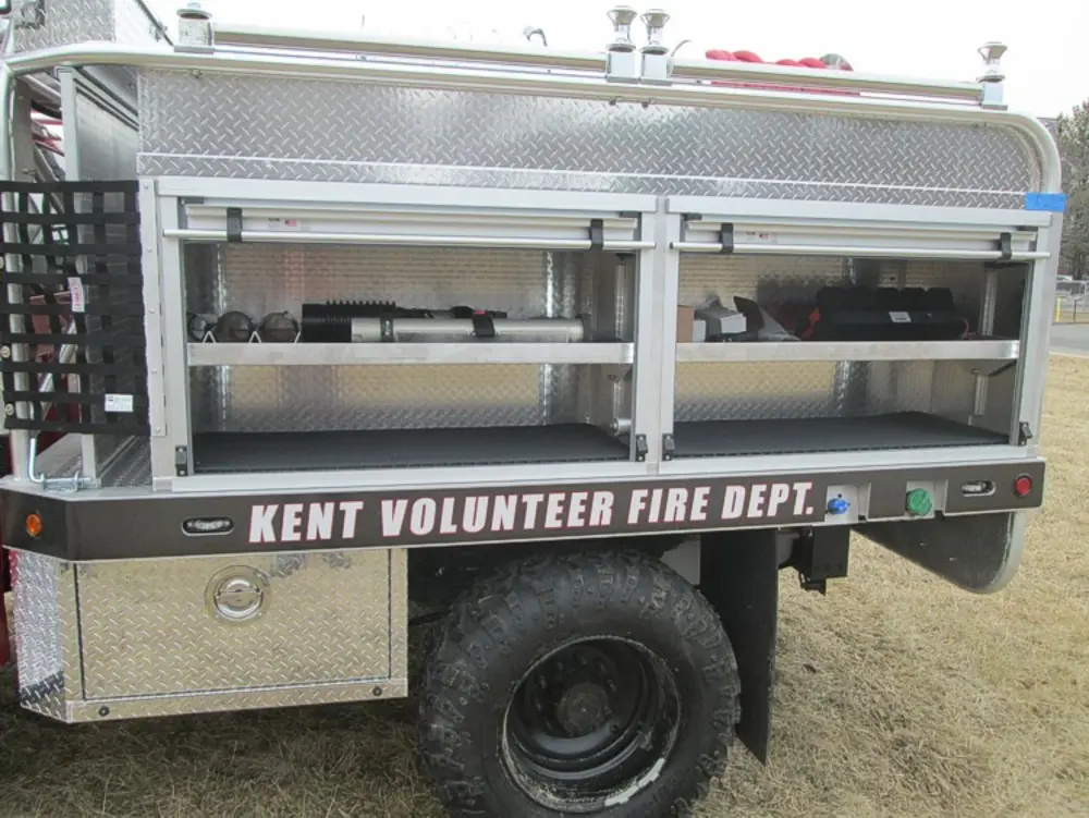 Exterior view of small fire truck showing cab, body compartments, and wheel/tire area.