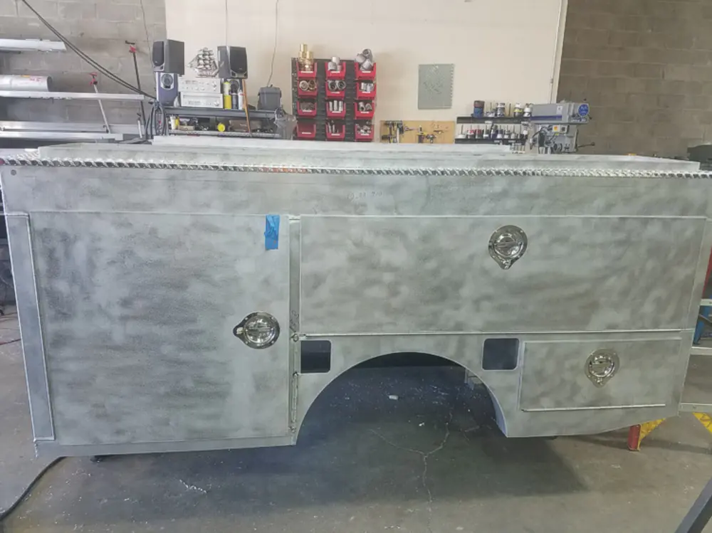 Exterior view of small fire truck showing cab, body compartments, and wheel/tire area.