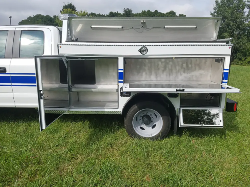Exterior view of small fire truck showing cab, body compartments, and wheel/tire area.