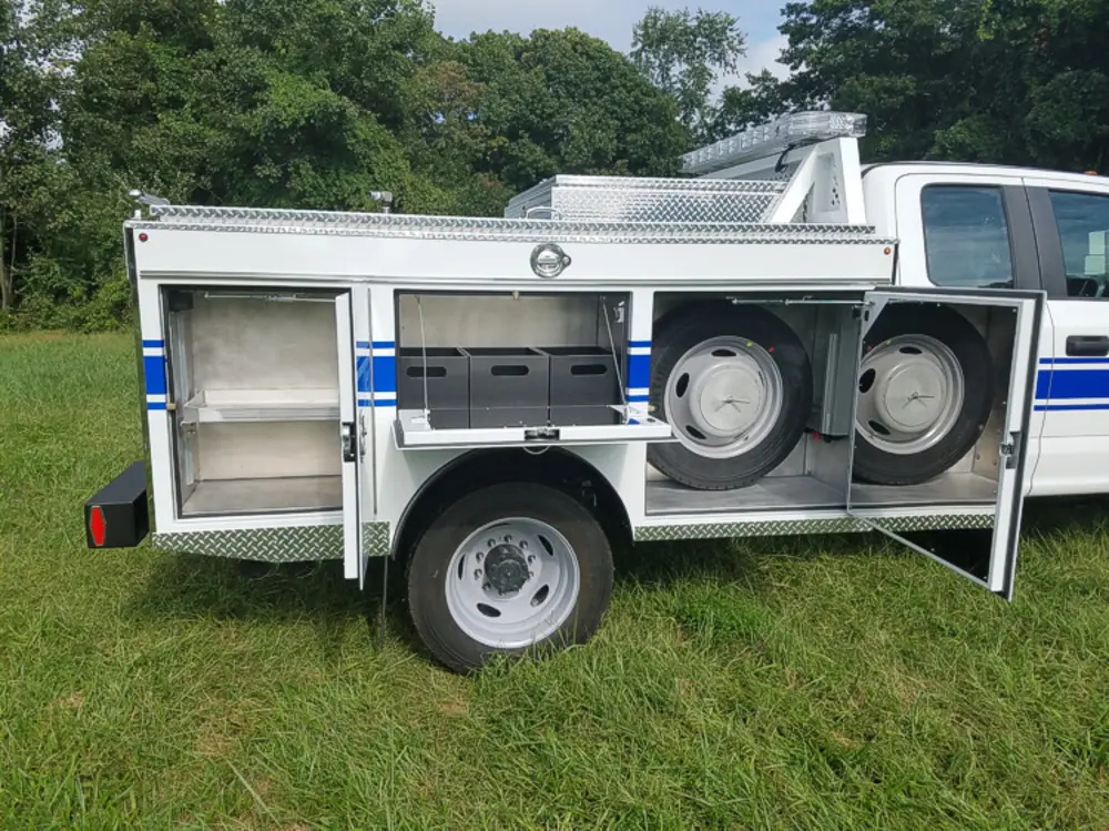 Exterior view of small fire truck showing cab, body compartments, and wheel/tire area.