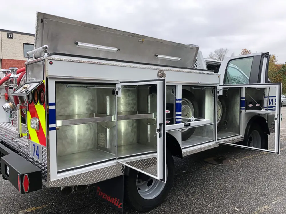 Exterior view of small fire truck showing cab, body compartments, and wheel/tire area.