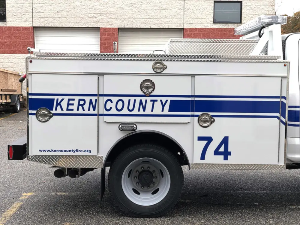 Exterior view of small fire truck showing cab, body compartments, and wheel/tire area.
