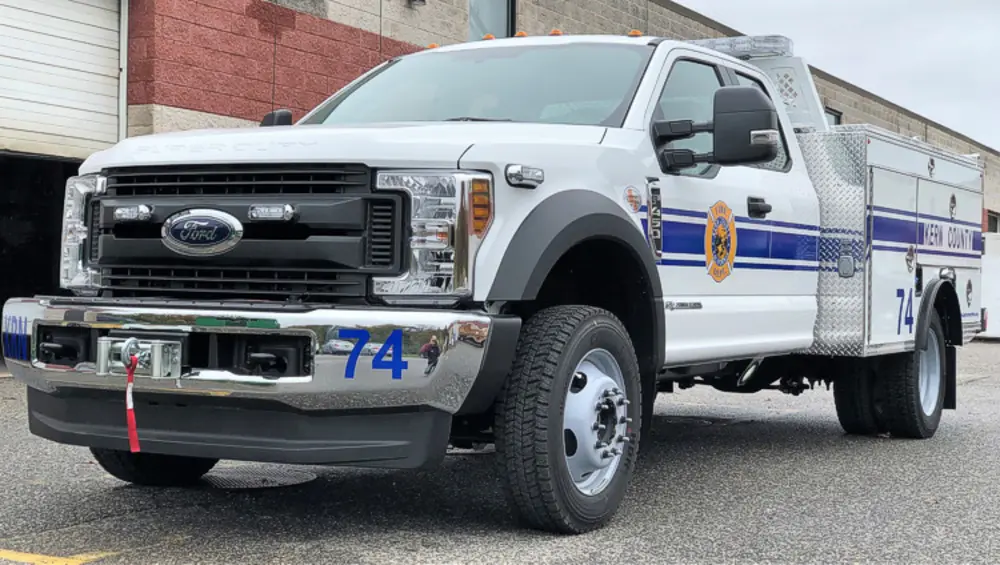 Exterior view of small fire truck showing cab, body compartments, and wheel/tire area.