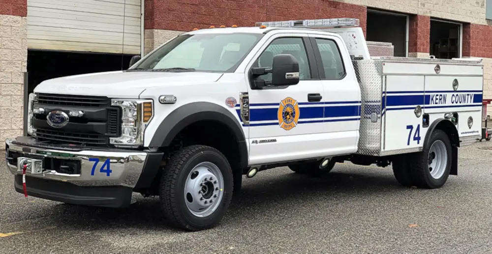 Exterior view of small fire truck showing cab, body compartments, and wheel/tire area.