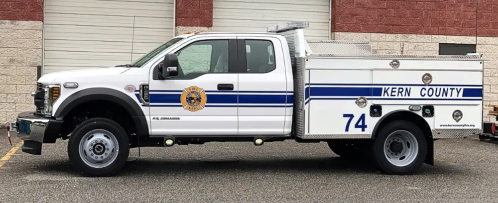 Exterior view of small fire truck showing cab, body compartments, and wheel/tire area.