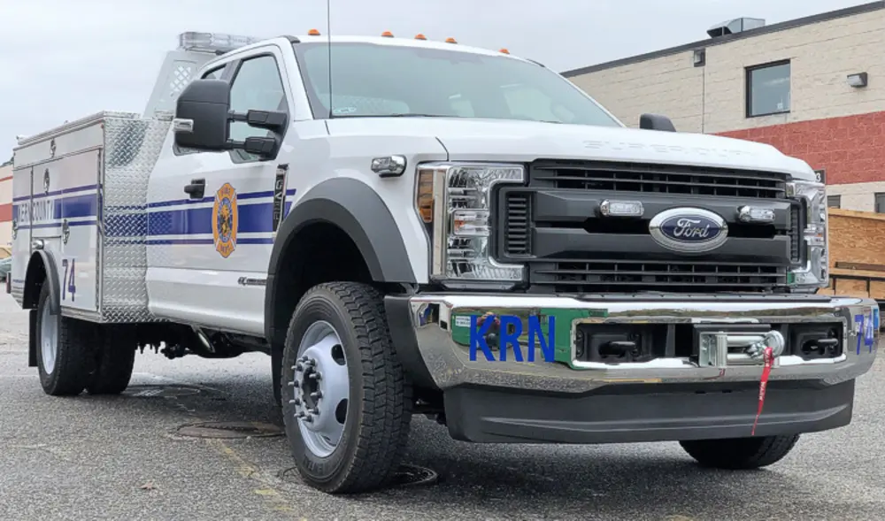 Exterior view of small fire truck showing cab, body compartments, and wheel/tire area.