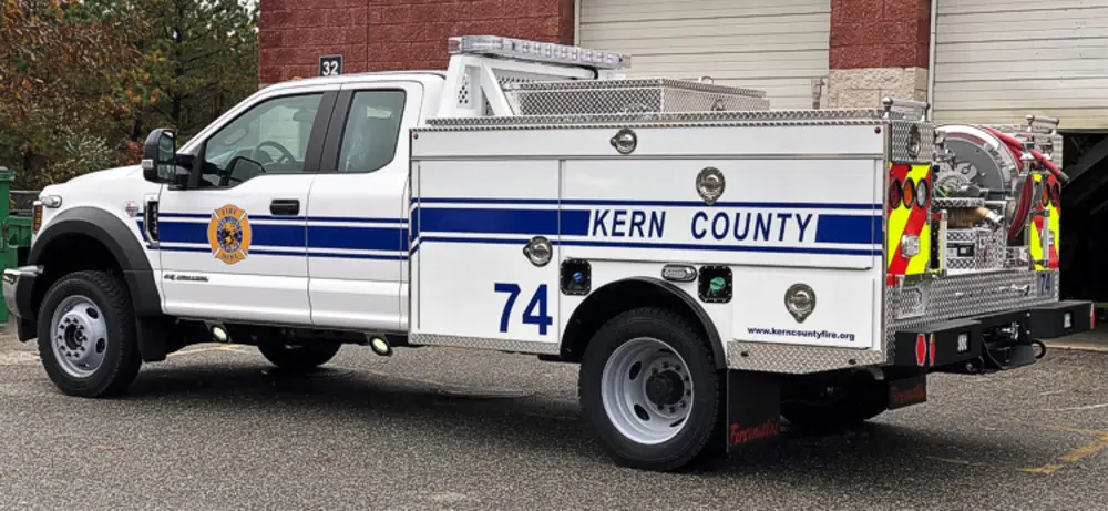 Exterior view of small fire truck showing cab, body compartments, and wheel/tire area.