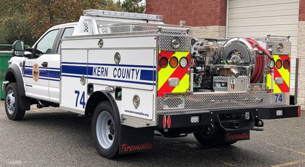 Exterior view of small fire truck showing cab, body compartments, and wheel/tire area.