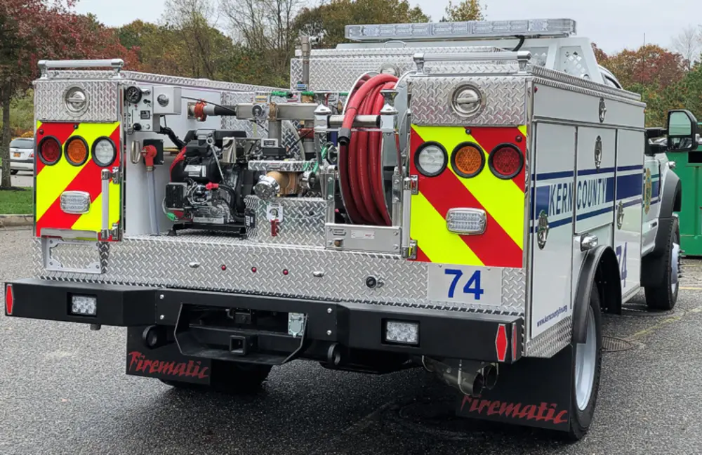 Exterior view of small fire truck showing cab, body compartments, and wheel/tire area.