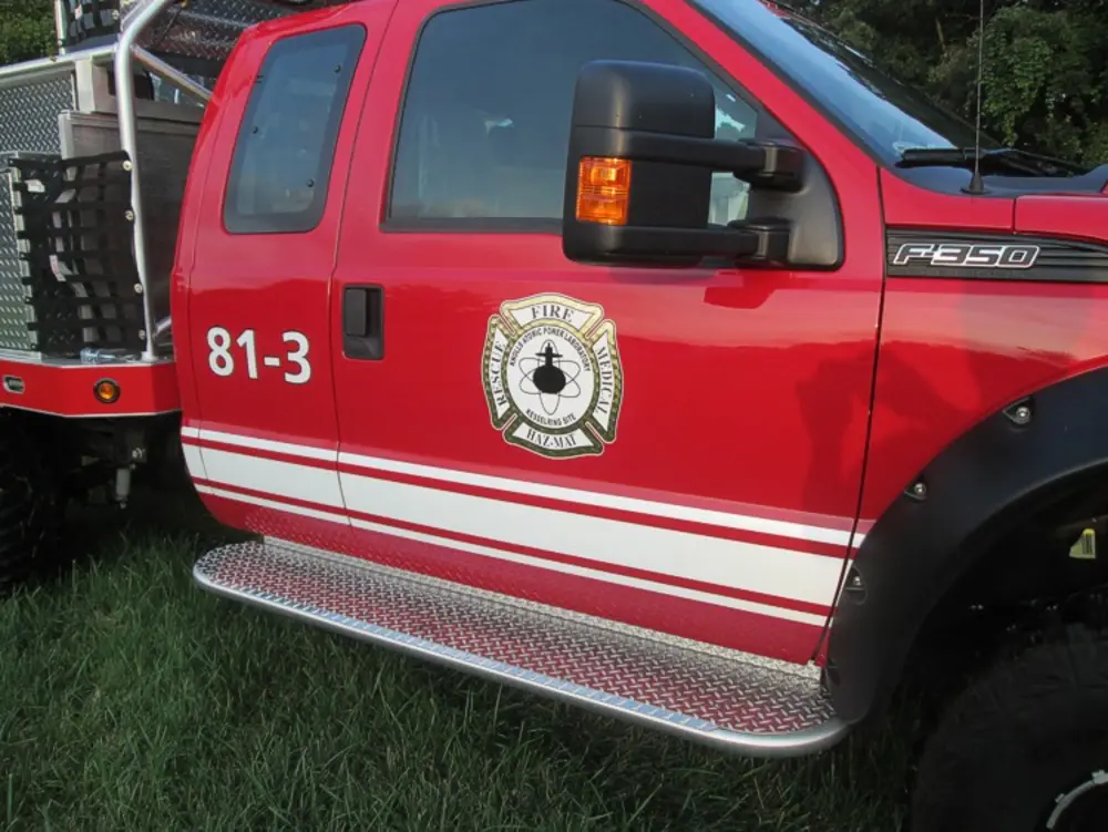 Exterior view of small fire truck showing cab, body compartments, and wheel/tire area.
