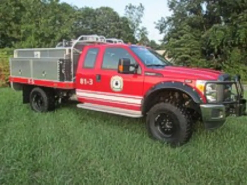 Exterior view of small fire truck showing cab, body compartments, and wheel/tire area.