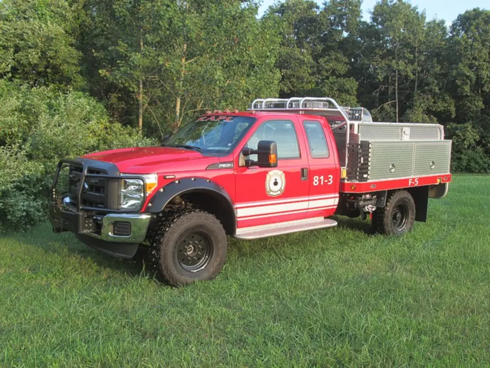 Exterior view of small fire truck showing cab, body compartments, and wheel/tire area.