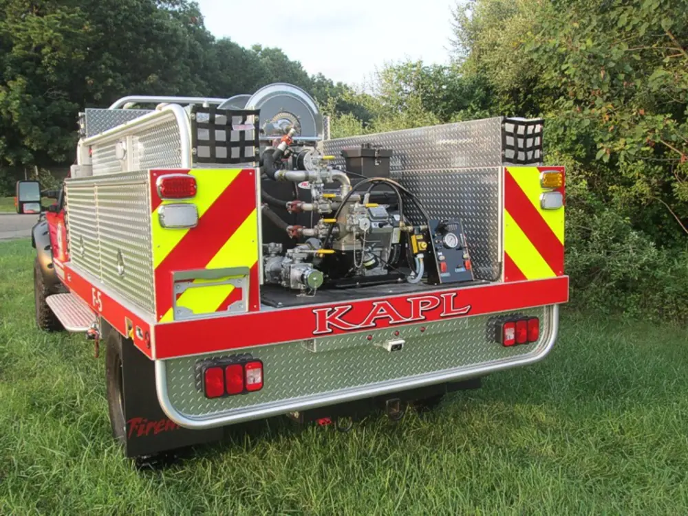 Exterior view of small fire truck showing cab, body compartments, and wheel/tire area.