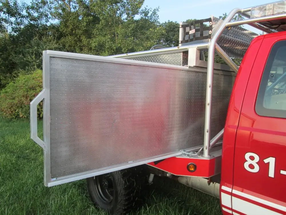 Exterior view of small fire truck showing cab, body compartments, and wheel/tire area.