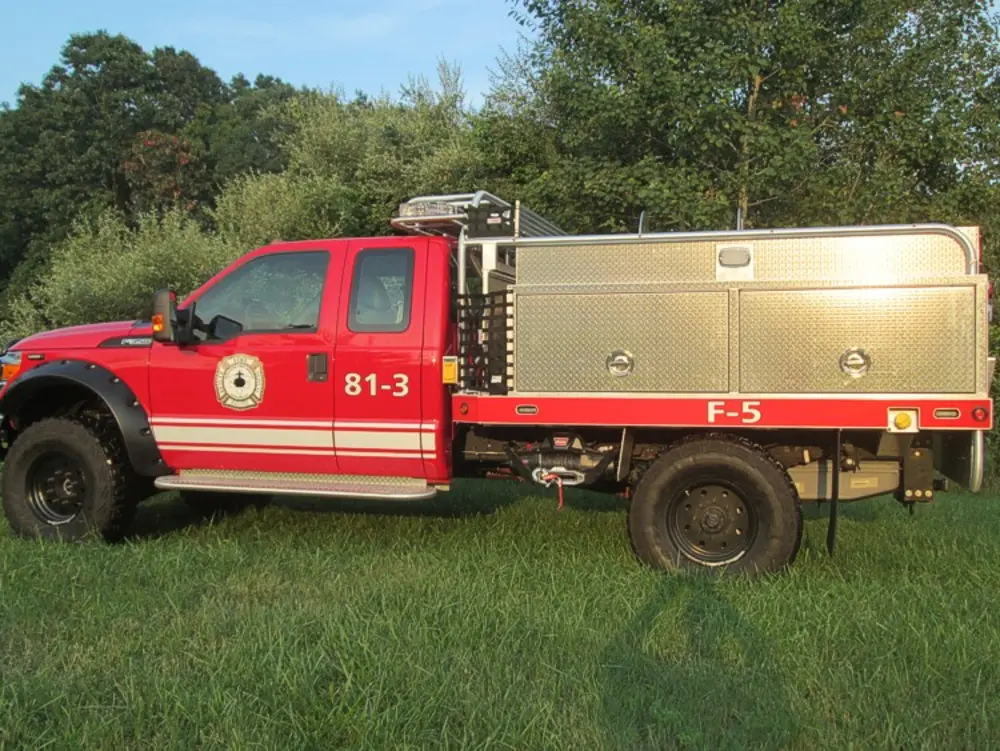 Exterior view of small fire truck showing cab, body compartments, and wheel/tire area.