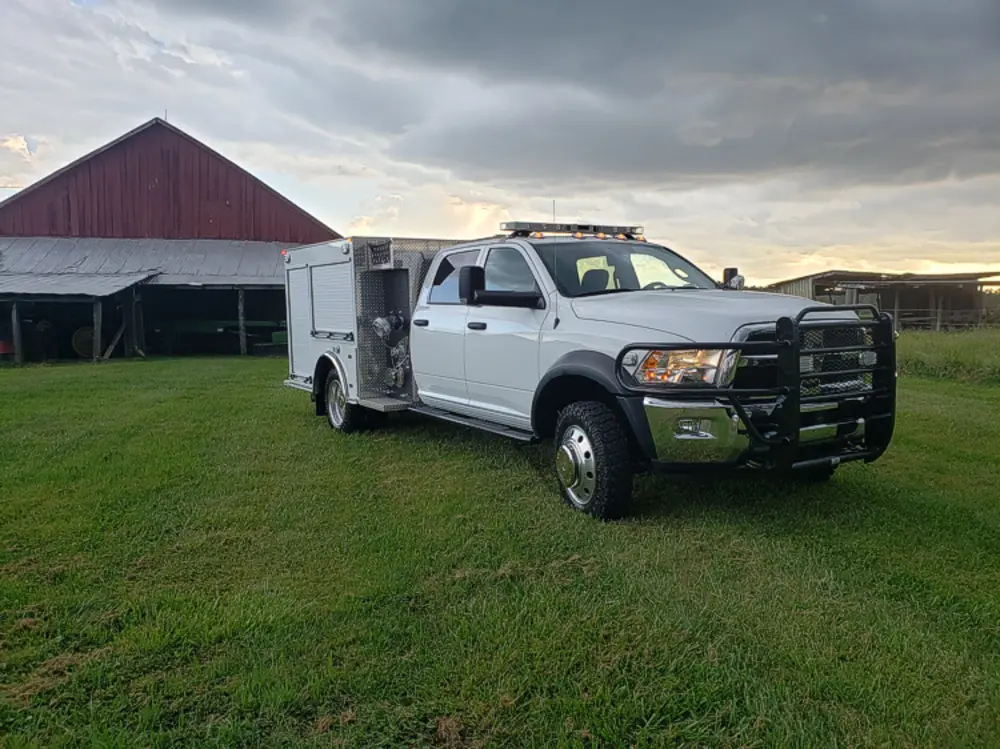 Exterior view of small fire truck showing cab, body compartments, and wheel/tire area.
