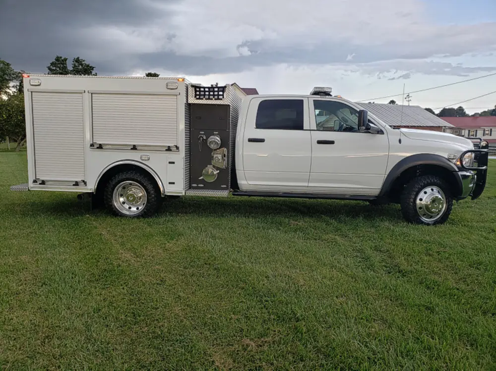 Exterior view of small fire truck showing cab, body compartments, and wheel/tire area.