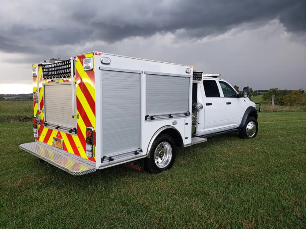 Exterior view of small fire truck showing cab, body compartments, and wheel/tire area.