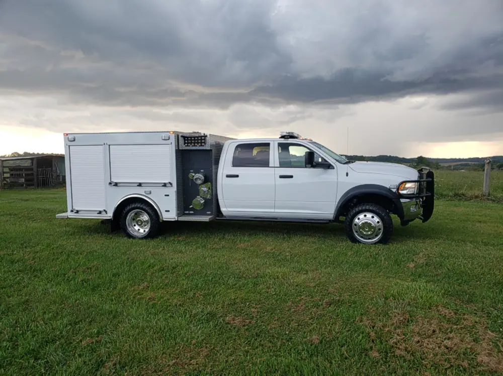 Exterior view of small fire truck showing cab, body compartments, and wheel/tire area.