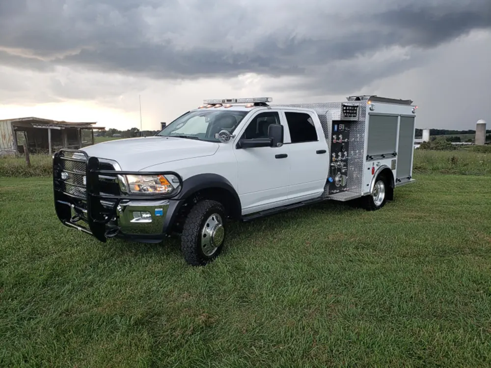 Exterior view of small fire truck showing cab, body compartments, and wheel/tire area.
