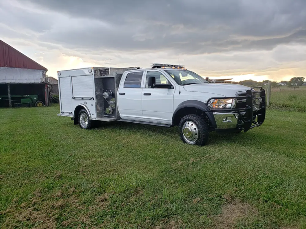 Exterior view of small fire truck showing cab, body compartments, and wheel/tire area.