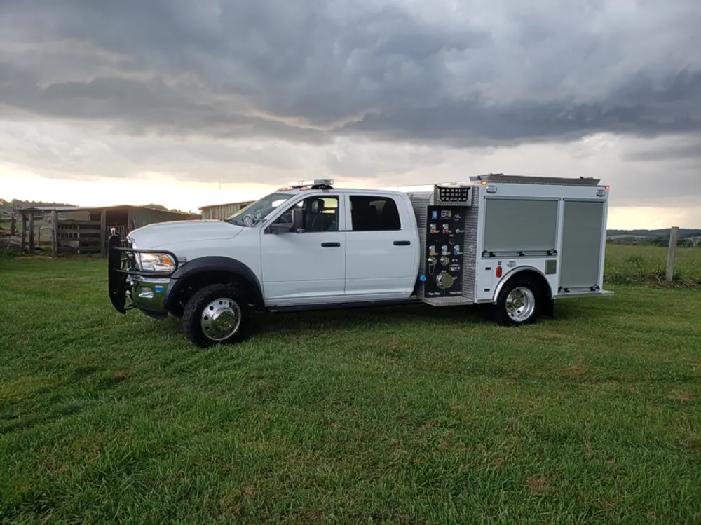 Exterior view of small fire truck showing cab, body compartments, and wheel/tire area.