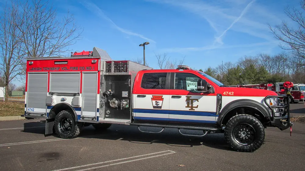 Exterior view of small fire truck showing cab, body compartments, and wheel/tire area.