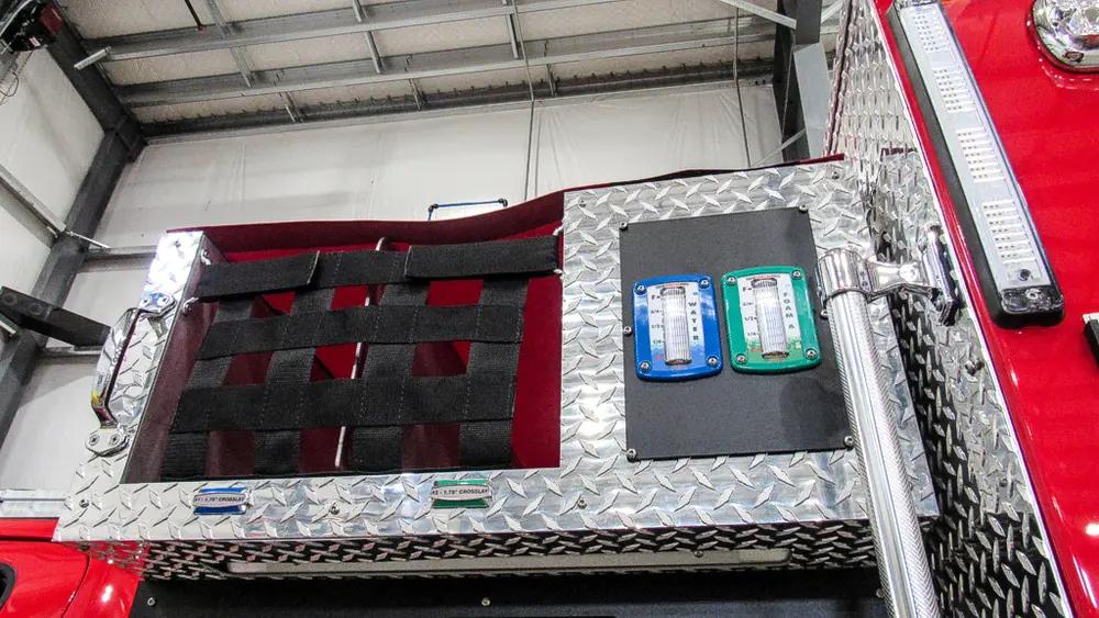 Exterior view of small fire truck showing cab, body compartments, and wheel/tire area.