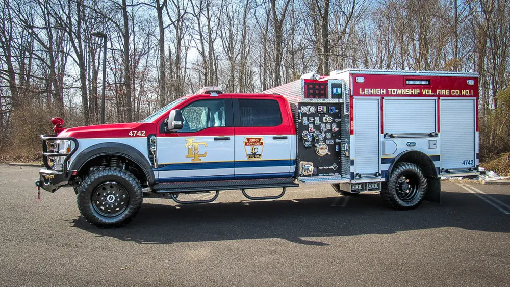 Exterior view of small fire truck showing cab, body compartments, and wheel/tire area.