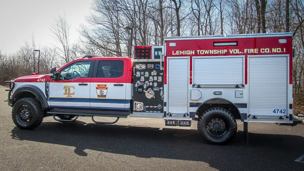 Exterior view of small fire truck showing cab, body compartments, and wheel/tire area.