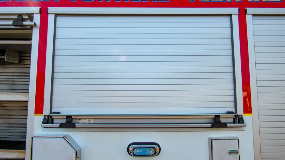 Exterior view of small fire truck showing cab, body compartments, and wheel/tire area.