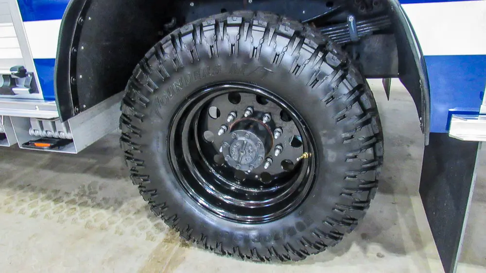 Exterior view of small fire truck showing cab, body compartments, and wheel/tire area.