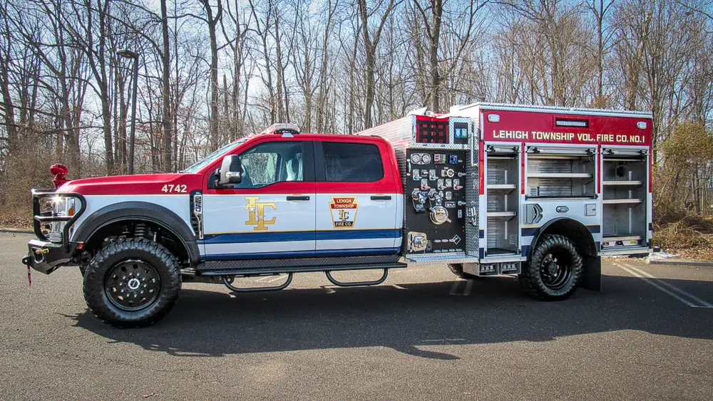Exterior view of small fire truck showing cab, body compartments, and wheel/tire area.