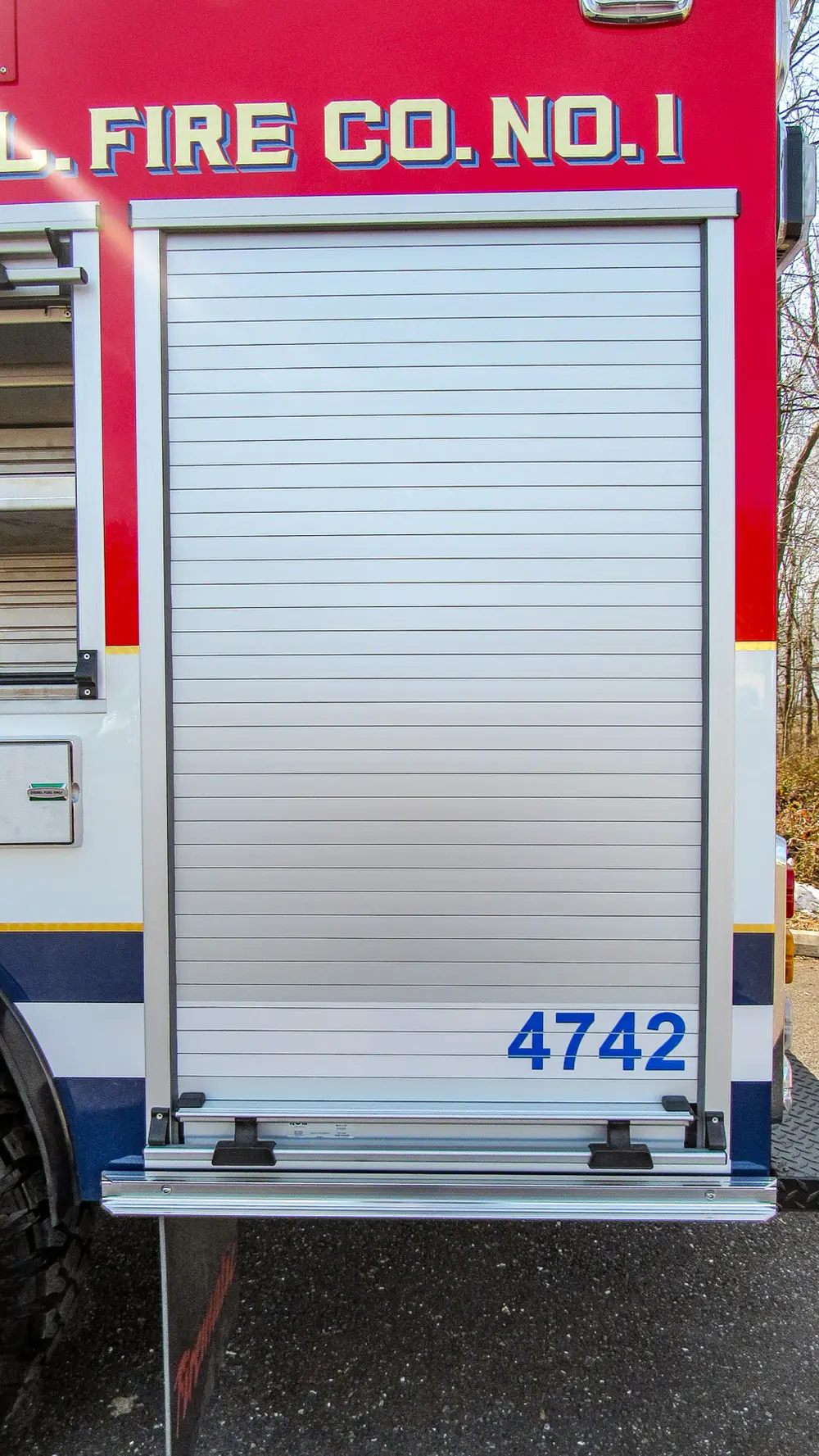 Exterior view of small fire truck showing cab, body compartments, and wheel/tire area.